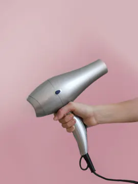 Pembe zemin önünde elde tutulan gümüş renkli fön makinesi